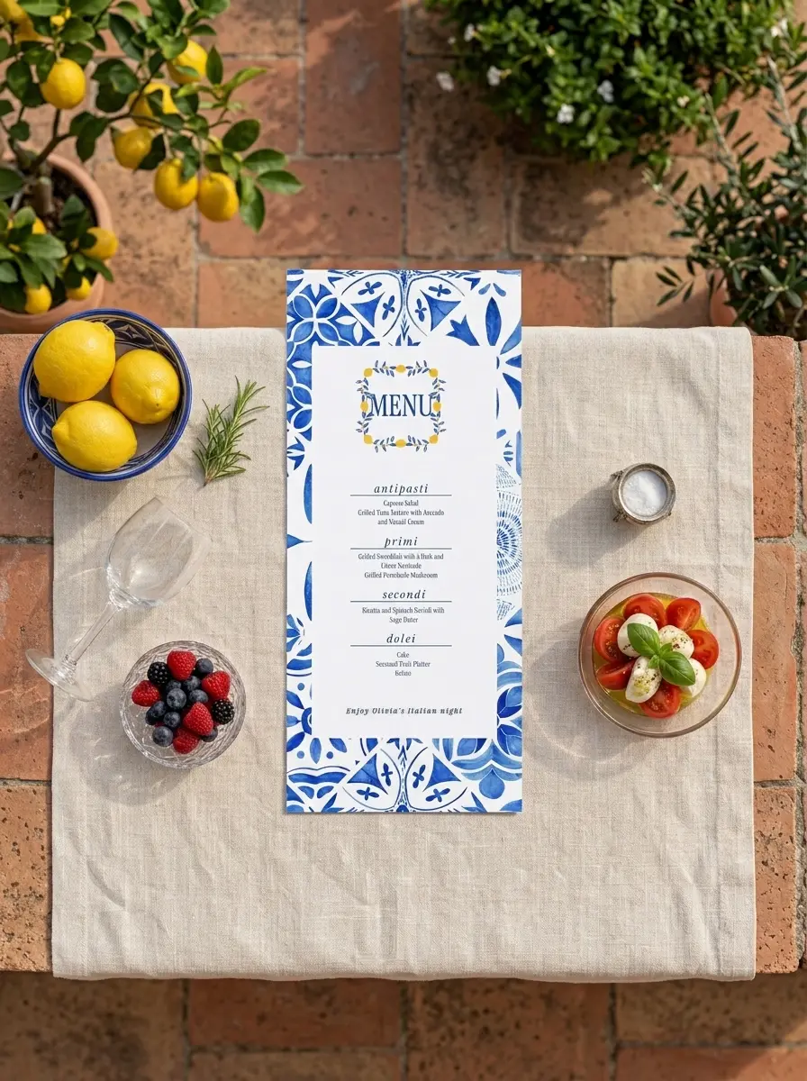 The printed Amalfi Blue menu lying on cream linen over a terracotta table, among lemons in a blue bowl, a caprese salad and fresh berries
